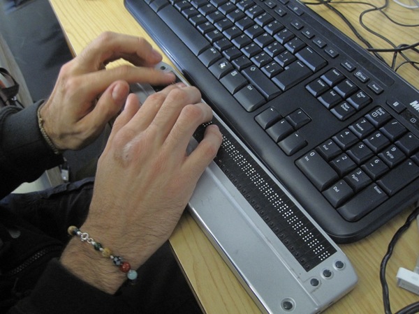 Egy felhasználó a hagyományos billentyűzet előtt elhelyezett Braille-kijelzőt tapogatja